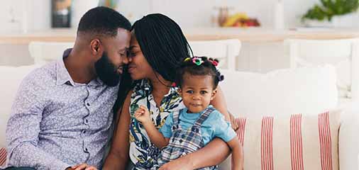 Black couple sitting on a couch with a young child on the mother’s lap - keatsagency.com