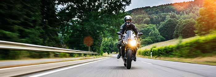 Motorcyclist riding a sportbike on a country road with trees and hills - keatsagency.com