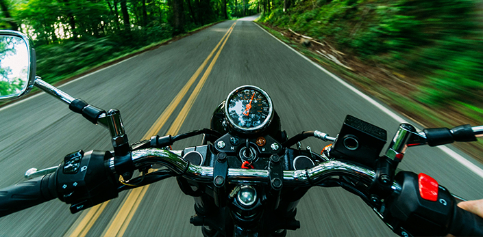 View over motorcycle handlebars on a tree-lined road - keatsagency.com