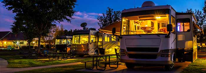 Parked motorhomes at a campground at dusk with interior lights on - keatsagency.com